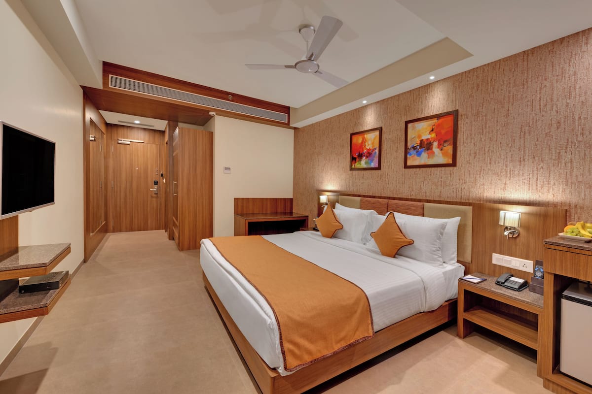 A hotel room with a large bed, a TV, a desk, and a small kitchenette.