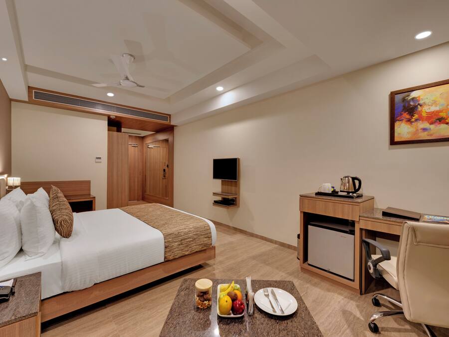 Quarto de hotel com cama, escrivaninha, cadeira, televisão e um quadro na parede.