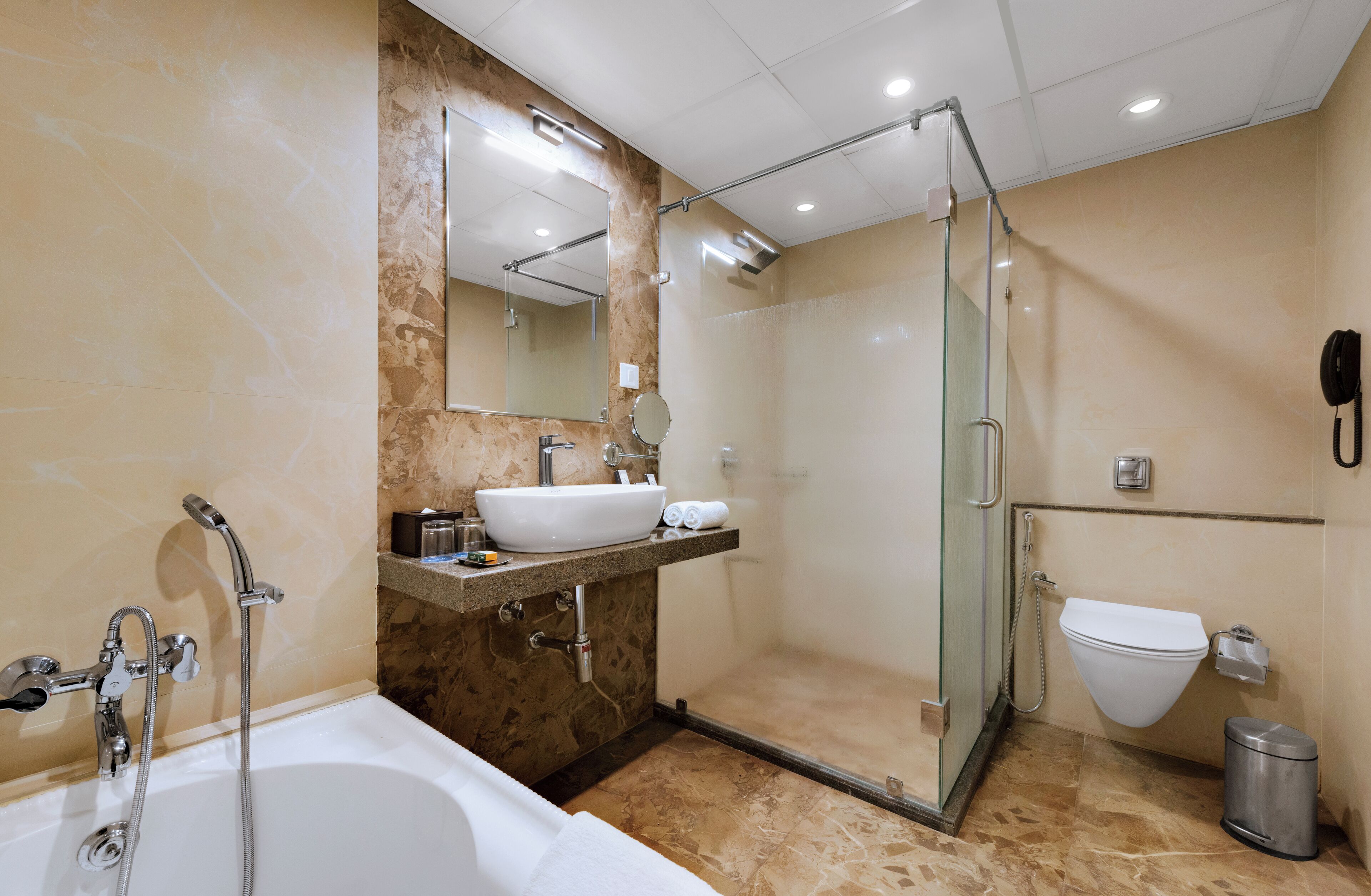 A modern bathroom with a bathtub, a glass-enclosed shower, a sink with a marble countertop, and a toilet.