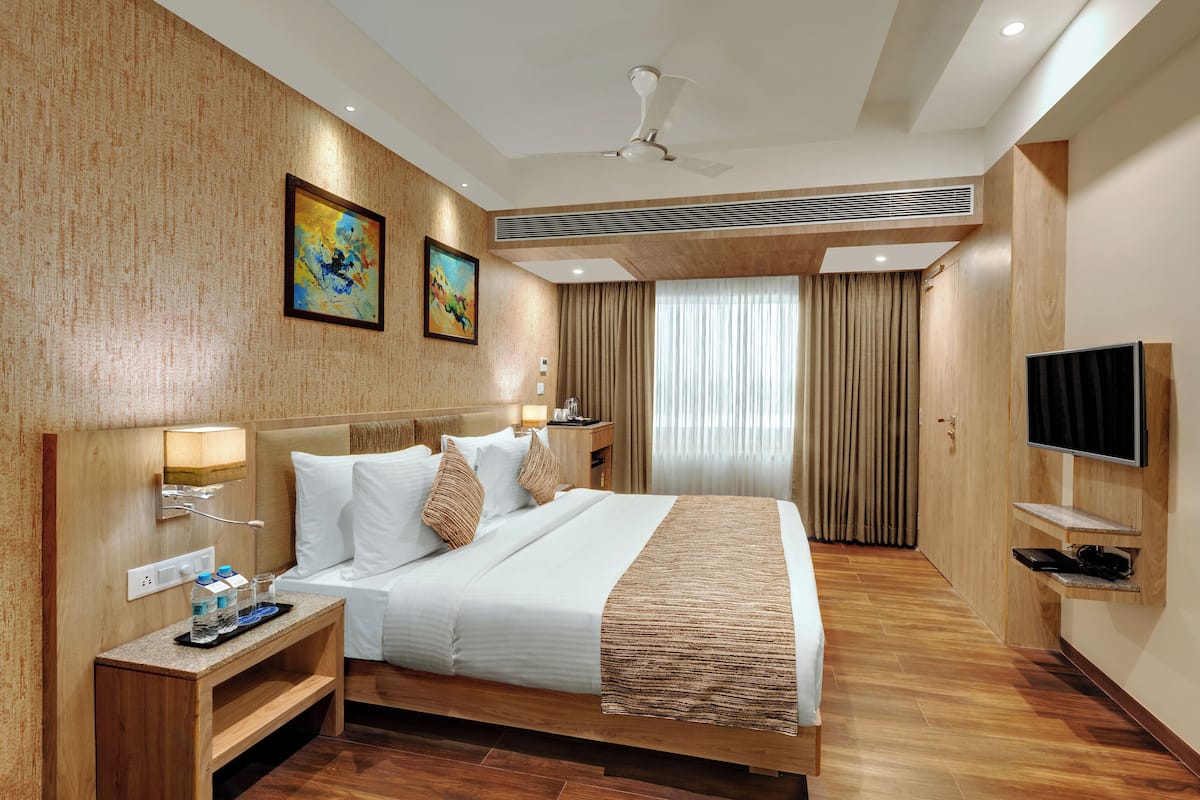 A modern hotel room with a large bed, a flat-screen TV, and a wooden floor.