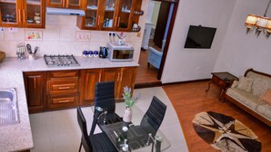 Une cuisine avec des meubles en bois, une table à manger avec des chaises, un four à micro-ondes et un téléviseur fixé au mur.