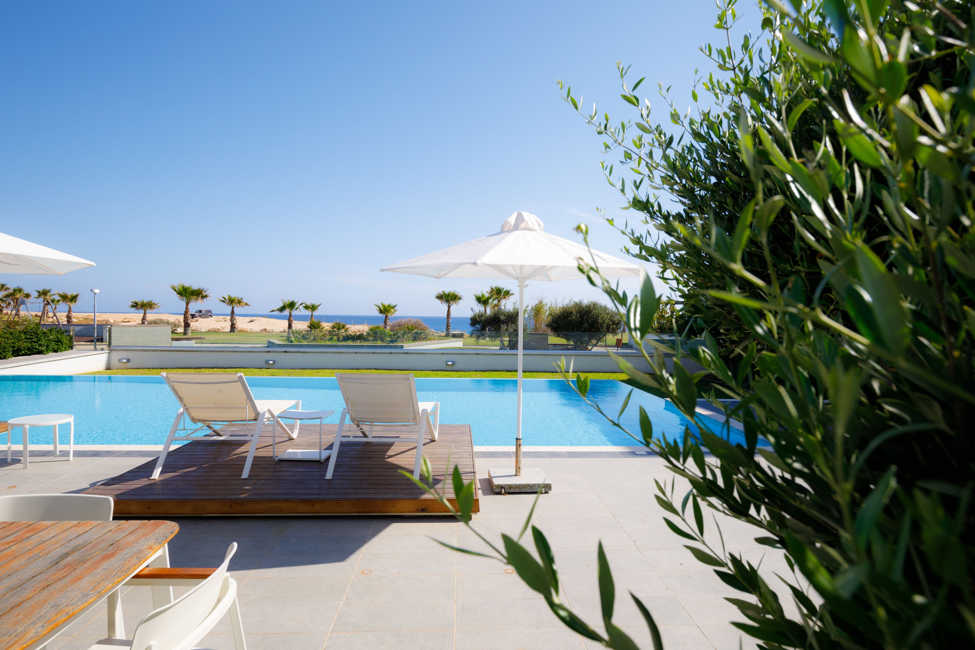 A poolside area with lounge chairs and umbrellas, a wooden deck, and a view of the beach and ocean.