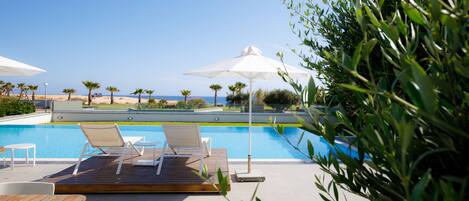 A poolside area with lounge chairs and umbrellas, a wooden deck, and a view of the beach and ocean.