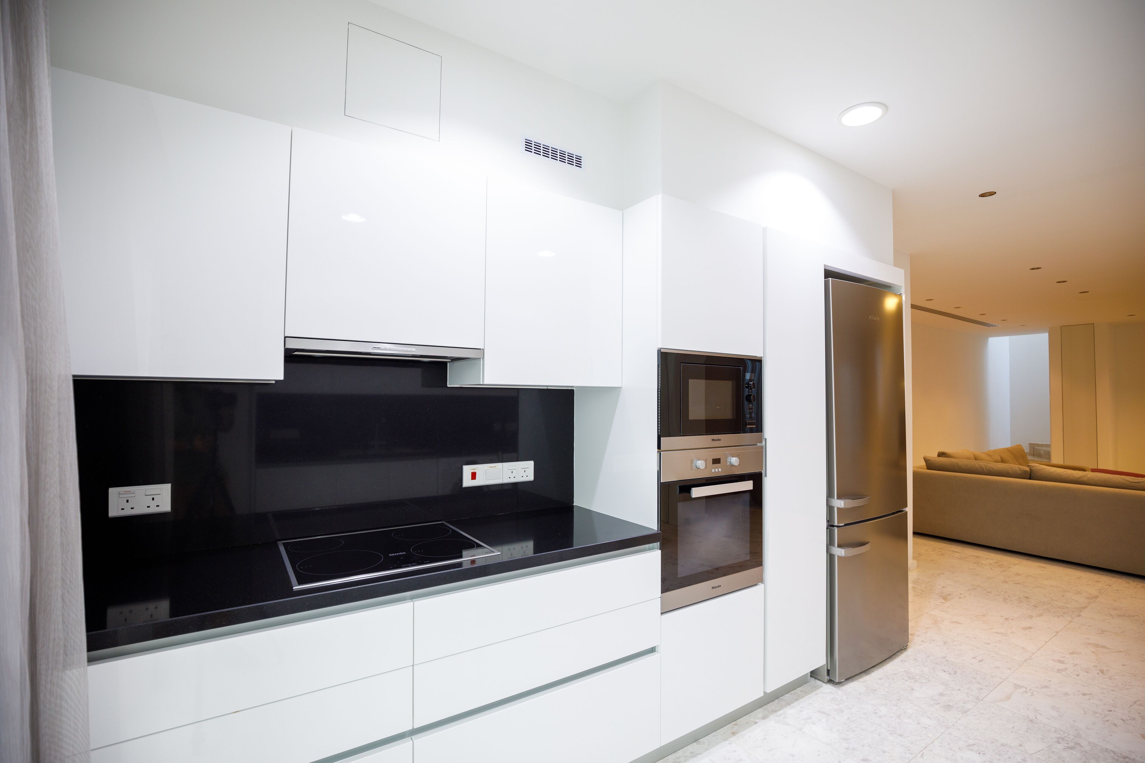 Een moderne keuken met witte kasten, een zwart aanrecht, een ingebouwde oven en een roestvrijstalen koelkast.