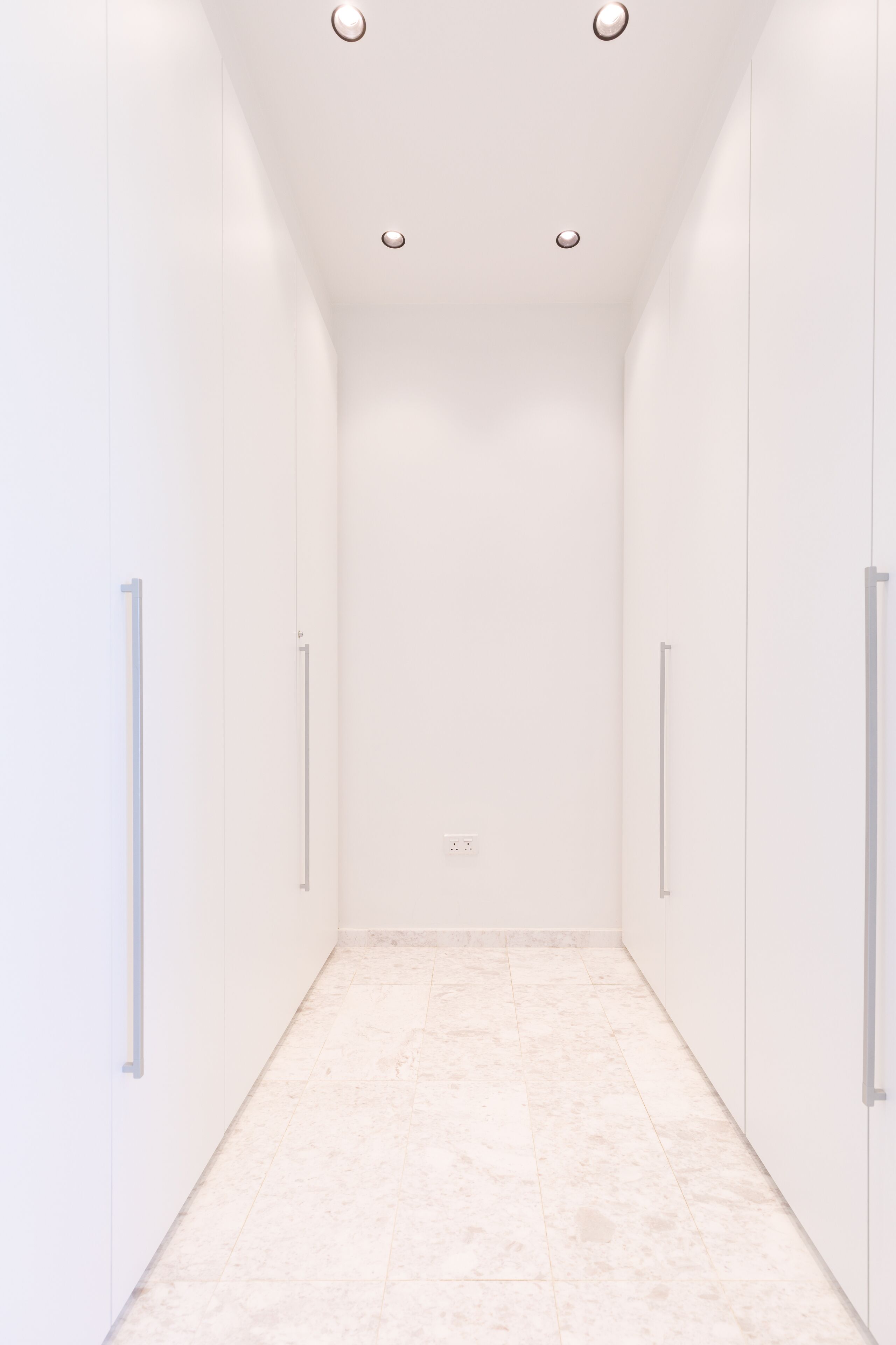 A narrow, white hallway with a tiled floor and a ceiling with recessed lighting.
