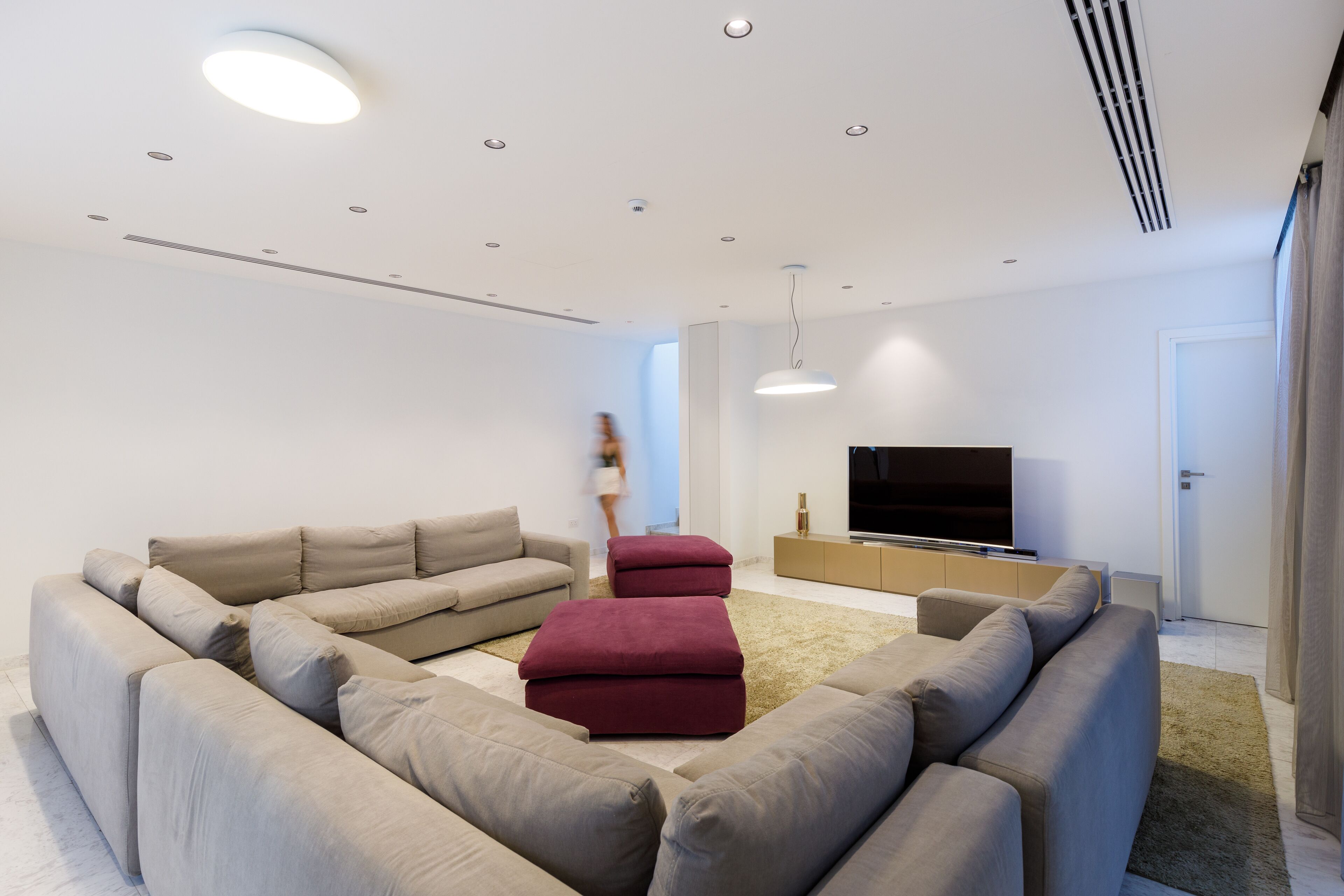 Una sala de estar moderna con un sofá modular, otomanas, un televisor de pantalla plana e iluminación empotrada en el techo.