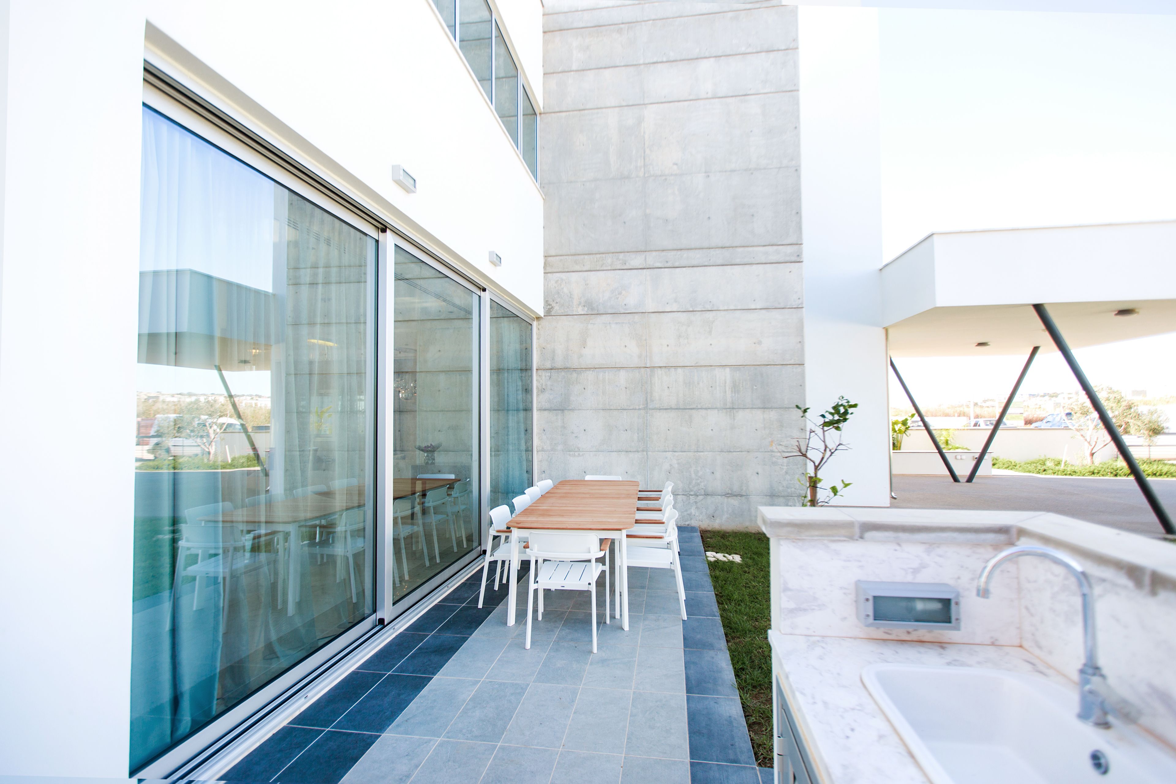 Eine moderne Außenpatio mit Esstisch und Stühlen, einer integrierten Spüle und einer Glastür zu einem Innenbereich.
