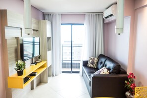 A modern living room with a flat-screen TV, a sofa with decorative pillows, a yellow console table, and a large window with curtains. - Landscape Diamond (Fortaleza)