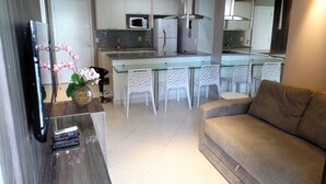A modern kitchen with a central island, white chairs, and a sofa. - Landscape Diamond (Fortaleza)