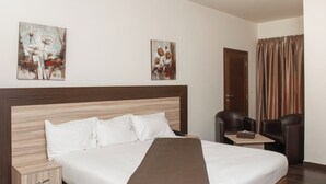 Een moderne hotelkamer met een groot bed, een houten nachtkastje, een bureau, twee stoelen en een kamerkleed met een patroon.