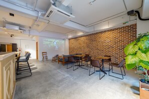 A modern conference room with a brick wall, a large screen, and a seating area with tables and chairs. - HOSTEL COCONE Kyoto - Station (Kyoto)