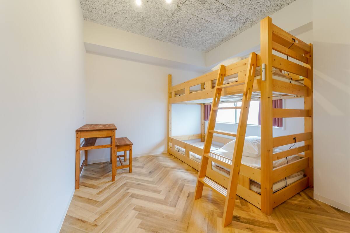 Ein Schlafzimmer mit Etagenbetten, einer Holzleiter, einem kleinen Holztisch und einem Holzboden mit Fischgrätmuster.