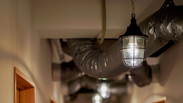 Un couloir avec des portes en bois, un luminaire suspendu et des conduits apparents.