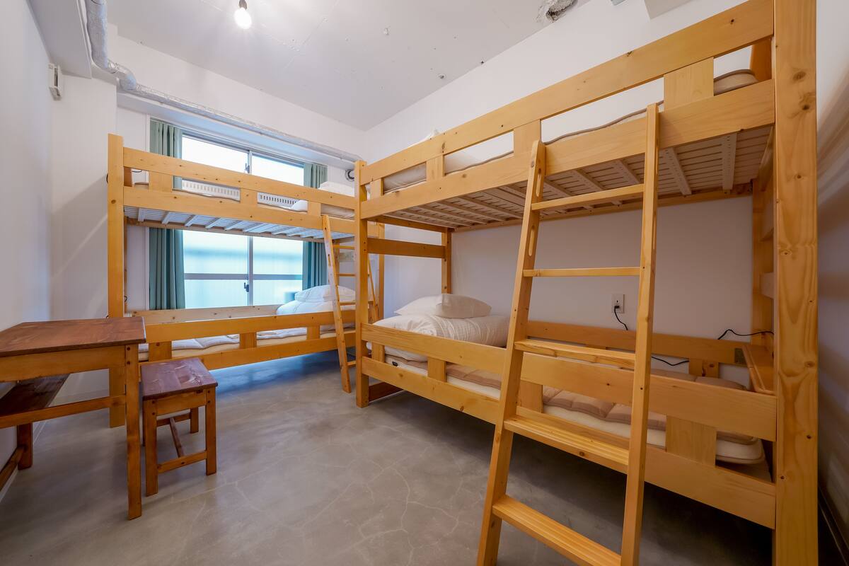 Ein Schlafsaalzimmer mit Etagenbetten, einem Holztisch und einem Fenster mit Vorhängen.