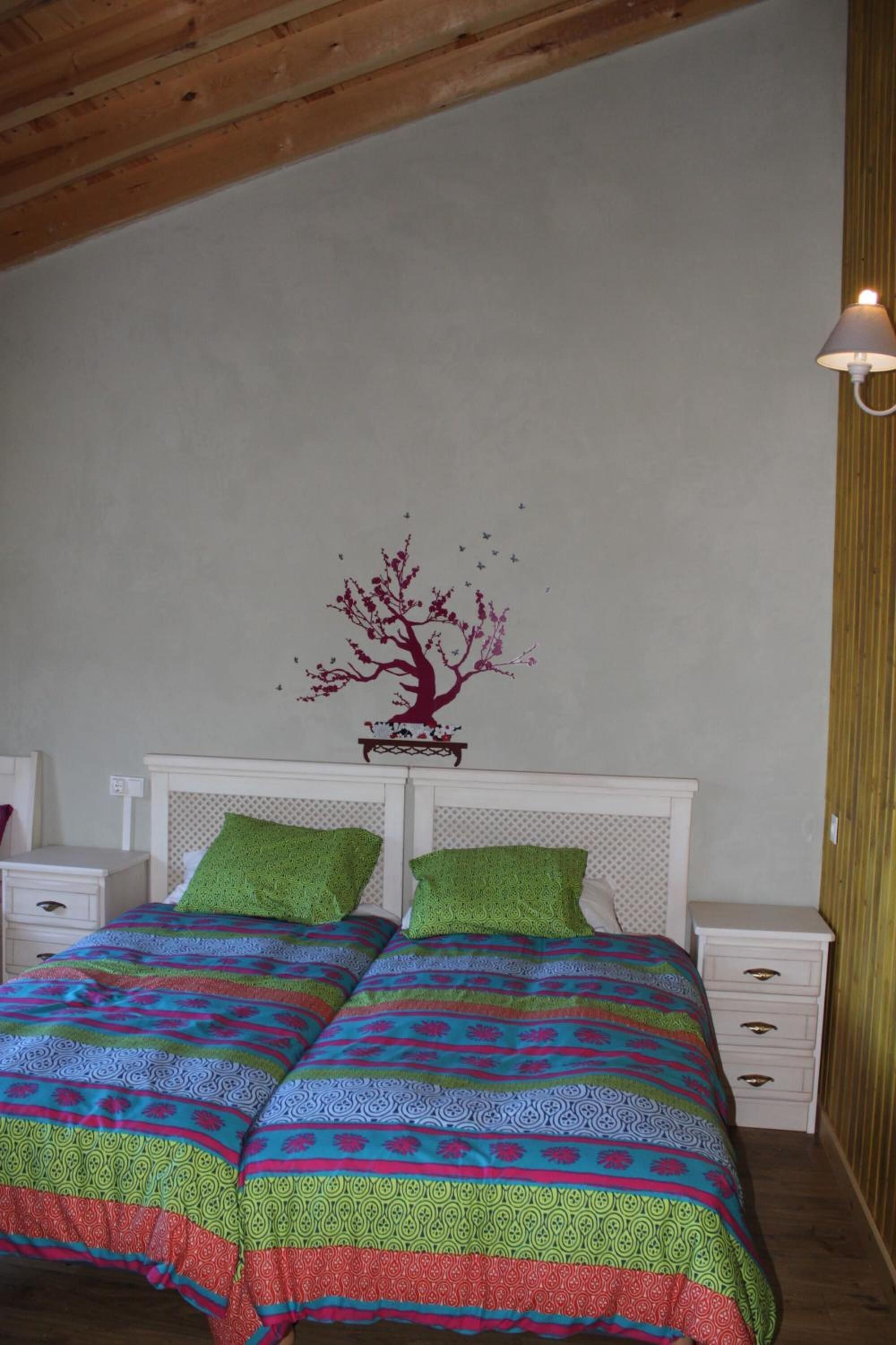 A bedroom with a bed, two nightstands, a lamp, and a wall decal of a tree.