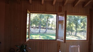 A wooden cabin with a large open window, a dining table, and a chair.