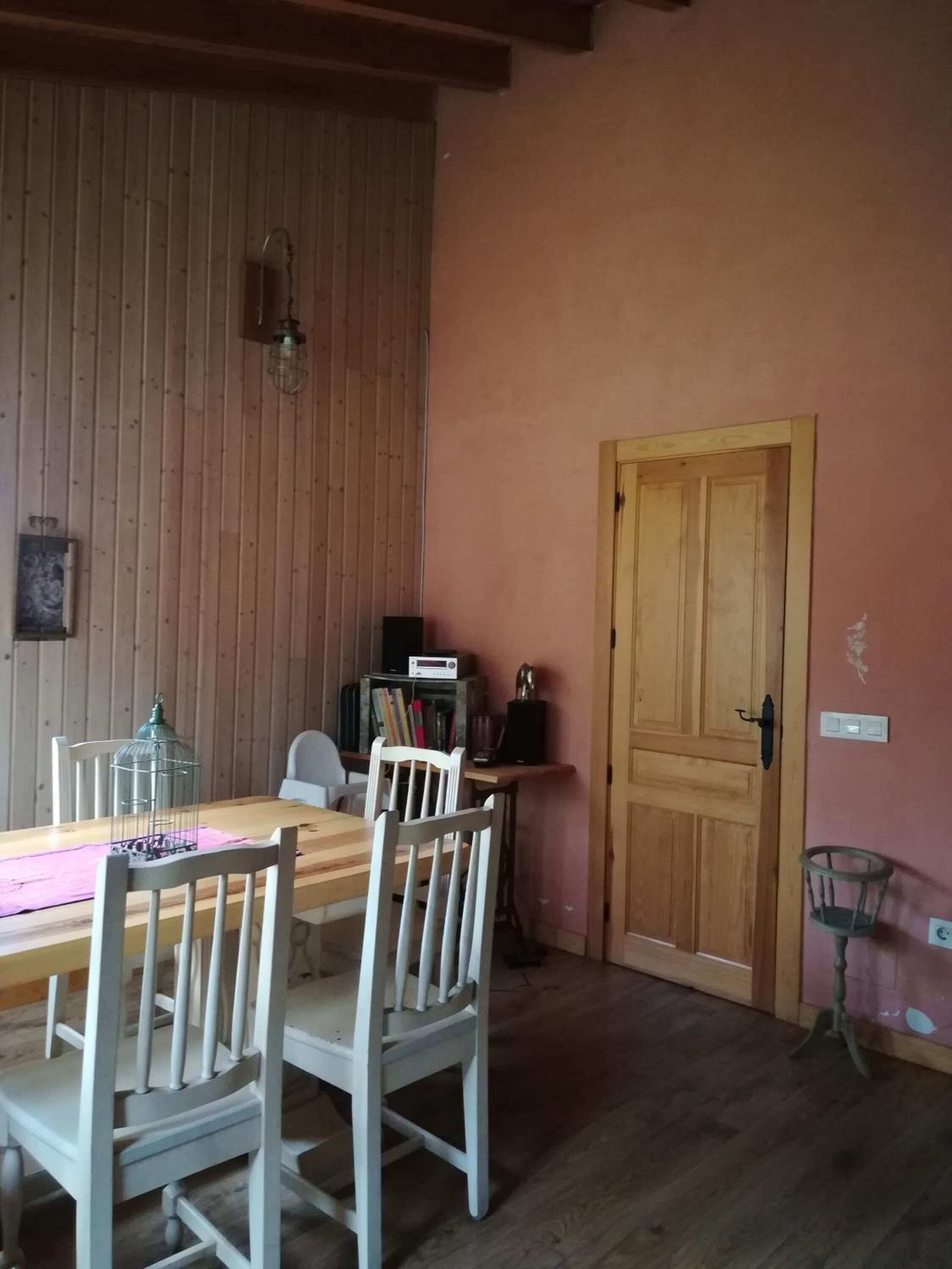 Een eethoek met een houten tafel, witte stoelen, een houten wand en een deur.