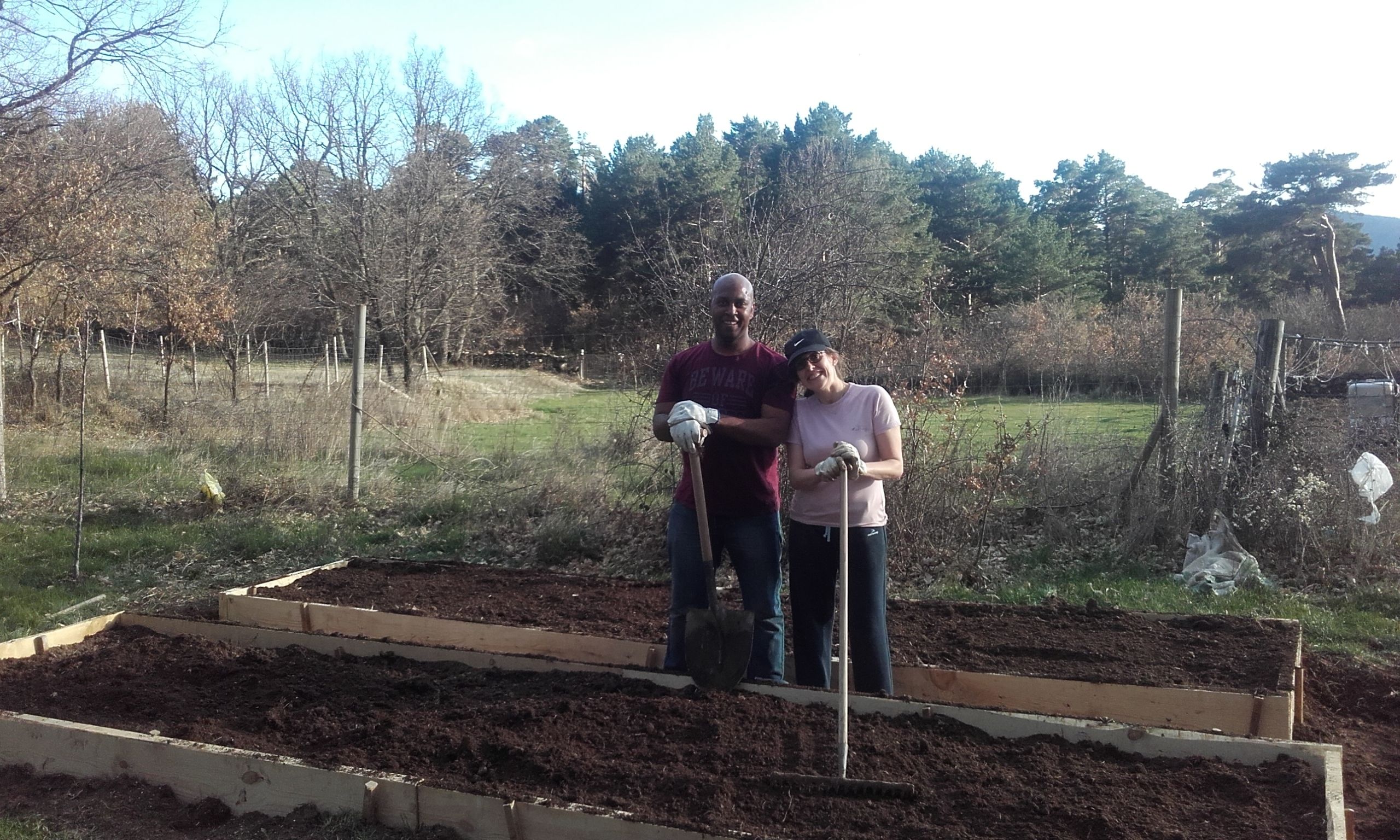Two people standing in a garden bed with wooden borders.