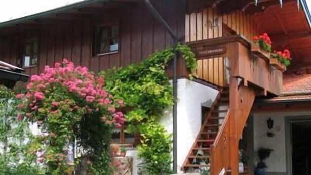 Uma casa de madeira com varanda, escadaria e jardim com flores cor-de-rosa.