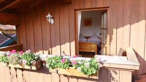 Uma cabana de madeira com uma cama e uma janela. Há caixas de flores com flores na parte externa.