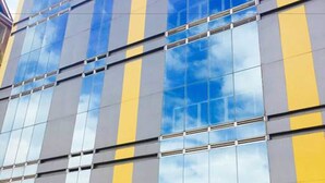 A modern building with a glass facade reflecting the sky and neighboring structures.