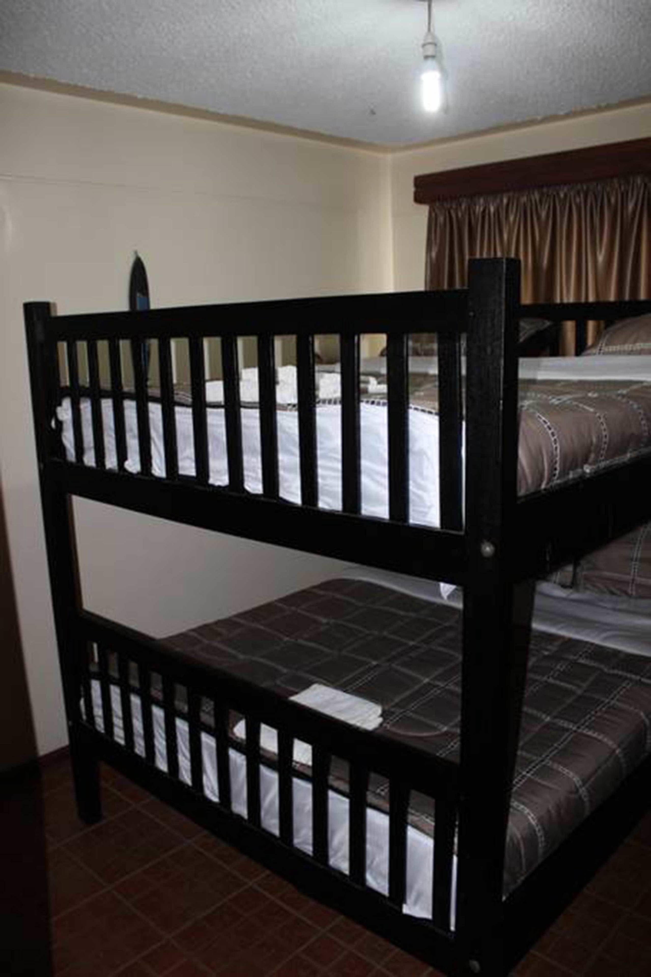 Ein Stockbett mit Kopfteil und Fußteil, ein Einzelbett mit gemustertem Bettbezug und ein Fenster mit Vorhängen.