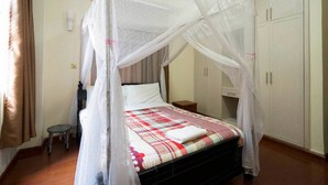 A bedroom with a bed under a mosquito net, a small stool, and a wardrobe.