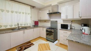 A compact kitchen with white cabinets, a gas stove, a microwave, and a kettle.