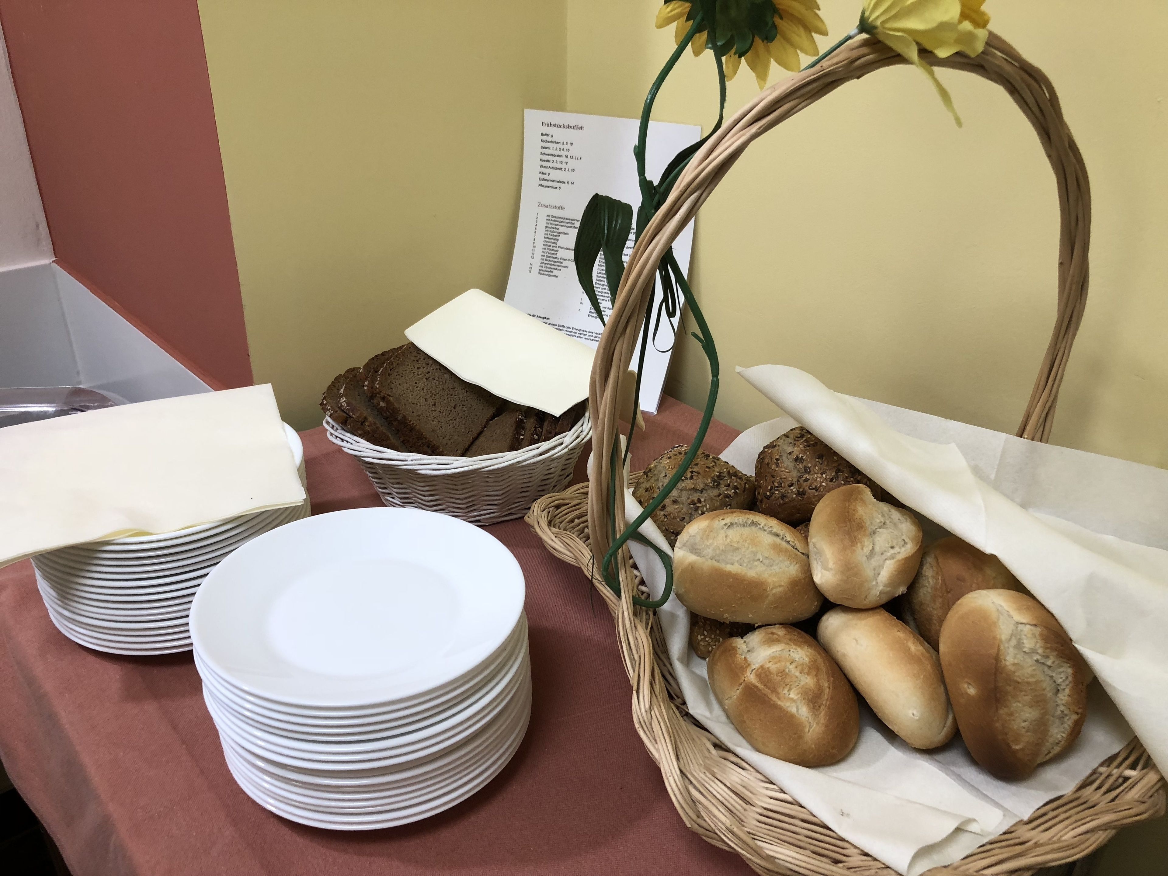 A table with stacks of white plates, a wicker basket with bread, and a menu.