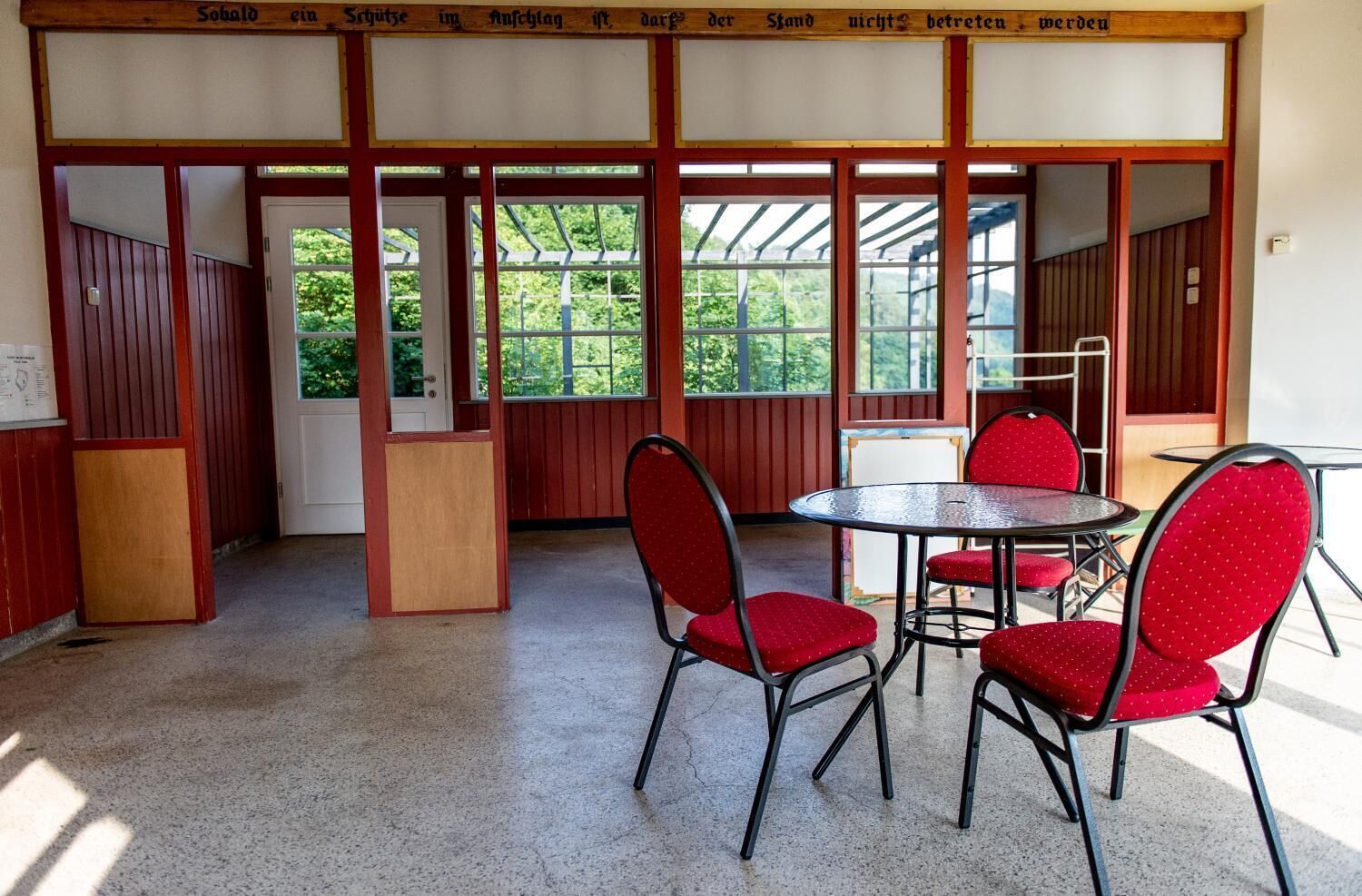 Una habitación con una mesa redonda y cuatro sillas rojas, paredes de madera y ventanas amplias.