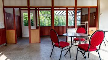 Una habitación con una mesa redonda y cuatro sillas rojas, paredes de madera y ventanas amplias.