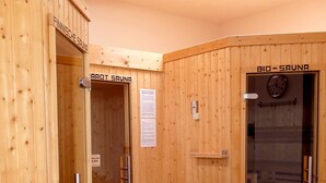 Une salle de sauna aux murs en bois, une porte portant l’inscription « SAUNA BIOLOGIQUE » et une horloge au mur.