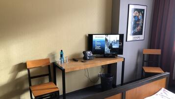 Una habitación de hotel con un escritorio de madera, un televisor, un teléfono y dos sillas de madera.