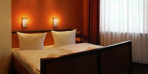 Ein Hotelzimmer mit einem Bett, zwei Wandleuchten, einem Nachttisch und einem mit Vorhängen versehenen Fenster.
