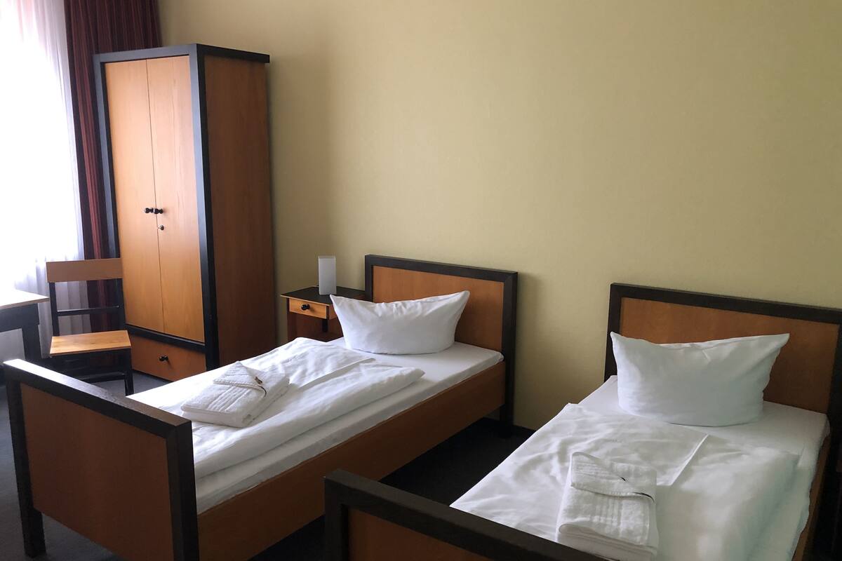 Habitació d'hotel amb dos llits individuals, un armari de fusta, un escriptori i una cadira.