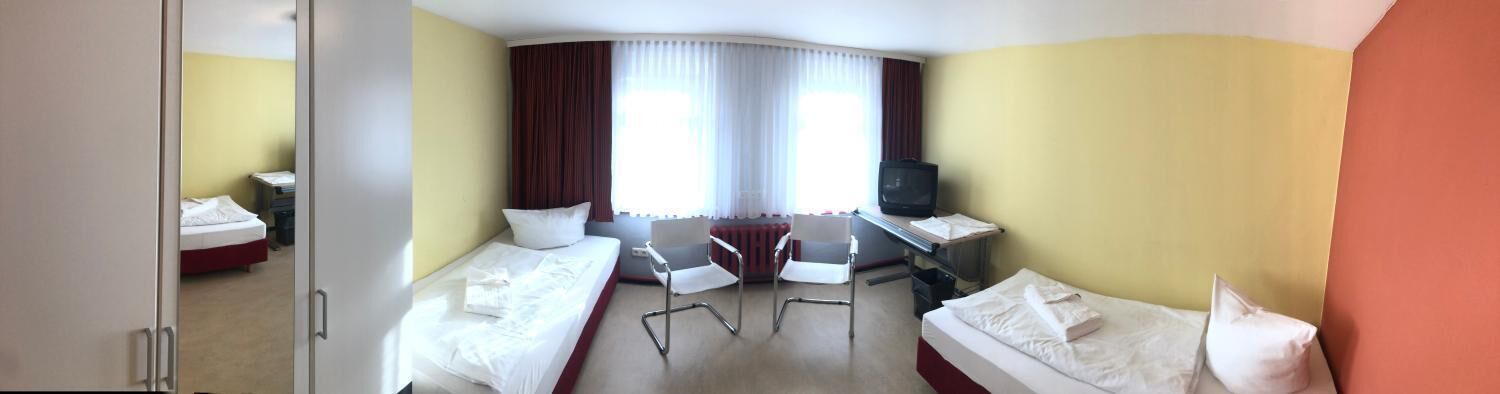 A hotel room with two beds, a desk with a computer, a chair, and a television.