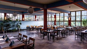 Un vaste espace dédié à la salle à manger, avec de nombreuses tables et chaises, de grandes fenêtres et des luminaires sphériques suspendus.
