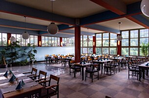 A spacious dining area with multiple tables and chairs, large windows, and hanging spherical light fixtures.