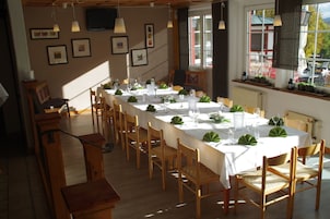 A dining area with a long table set for a meal, wooden chairs, and framed pictures on the wall.