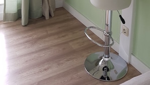 Una habitación de esquina con una pared verde claro, un estante blanco con una planta en maceta, un lavamanos pedestal blanco y suelo de madera.