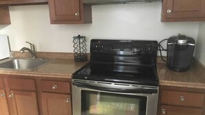 A kitchen with a stainless steel stove, a coffee maker, and wooden cabinets. - Geomara 2 Bdroom Ppl Center (Nairobi)