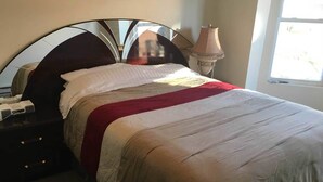 A neatly made bed with a red and white blanket, a bedside lamp, and a nightstand with a phone and a small box. - Geomara 2 Bdroom Ppl Center (Nairobi)
