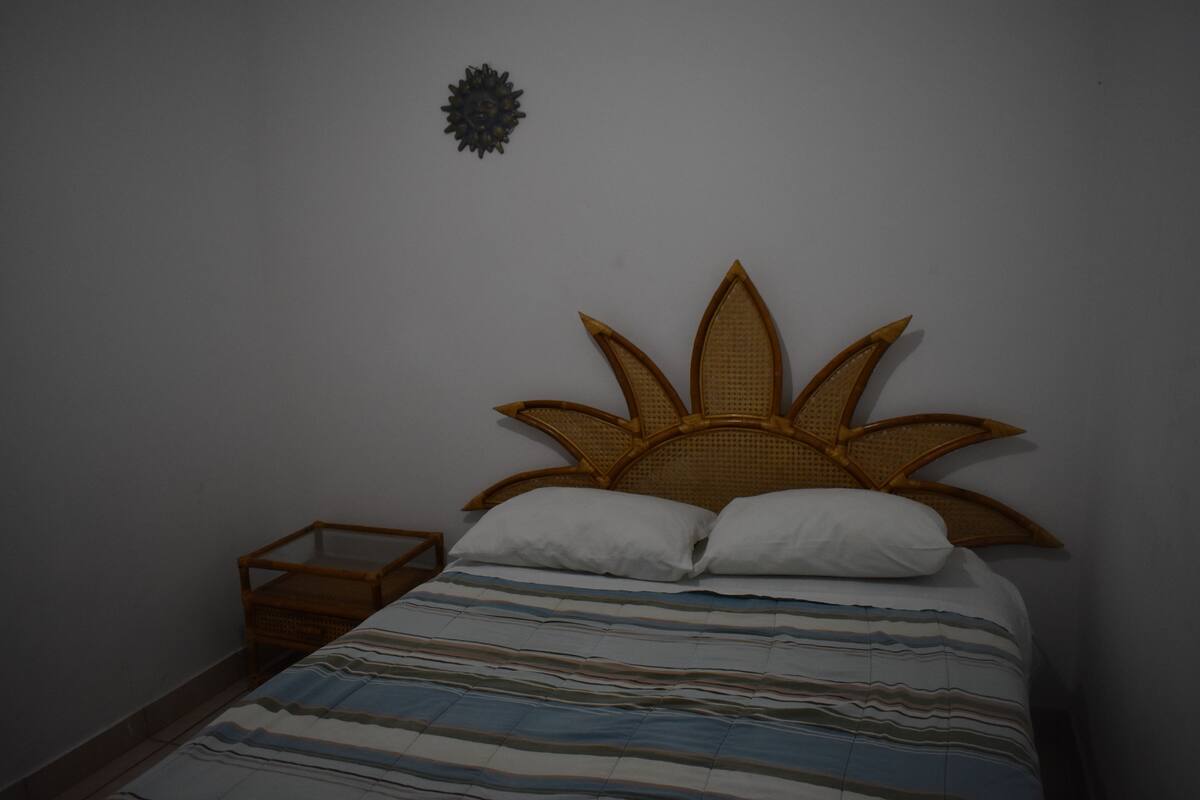Ein Bett mit einem gewobenen Kopfteil, einer gestreiften Tagesdecke und einem kleinen Nachttisch.
