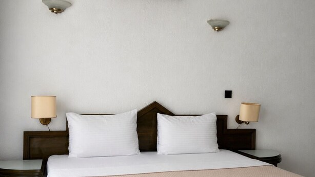 A hotel room with a bed, two bedside tables, a wall-mounted air conditioner, and two wall-mounted lamps. - Club Mel Holiday Resort (Ortaca)