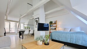 Een moderne slaapkamer in loftstijl, met een bed, een televisie en een zithoek met stoelen en een tafel.