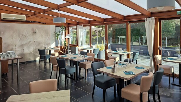 Un vaste espace de restauration intérieur agrémenté de poutres en bois, de grandes fenêtres, ainsi que de nombreuses tables et chaises.