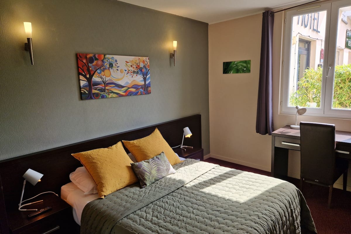 A hotel room with a bed, bedside lamps, a desk, and a window with curtains.