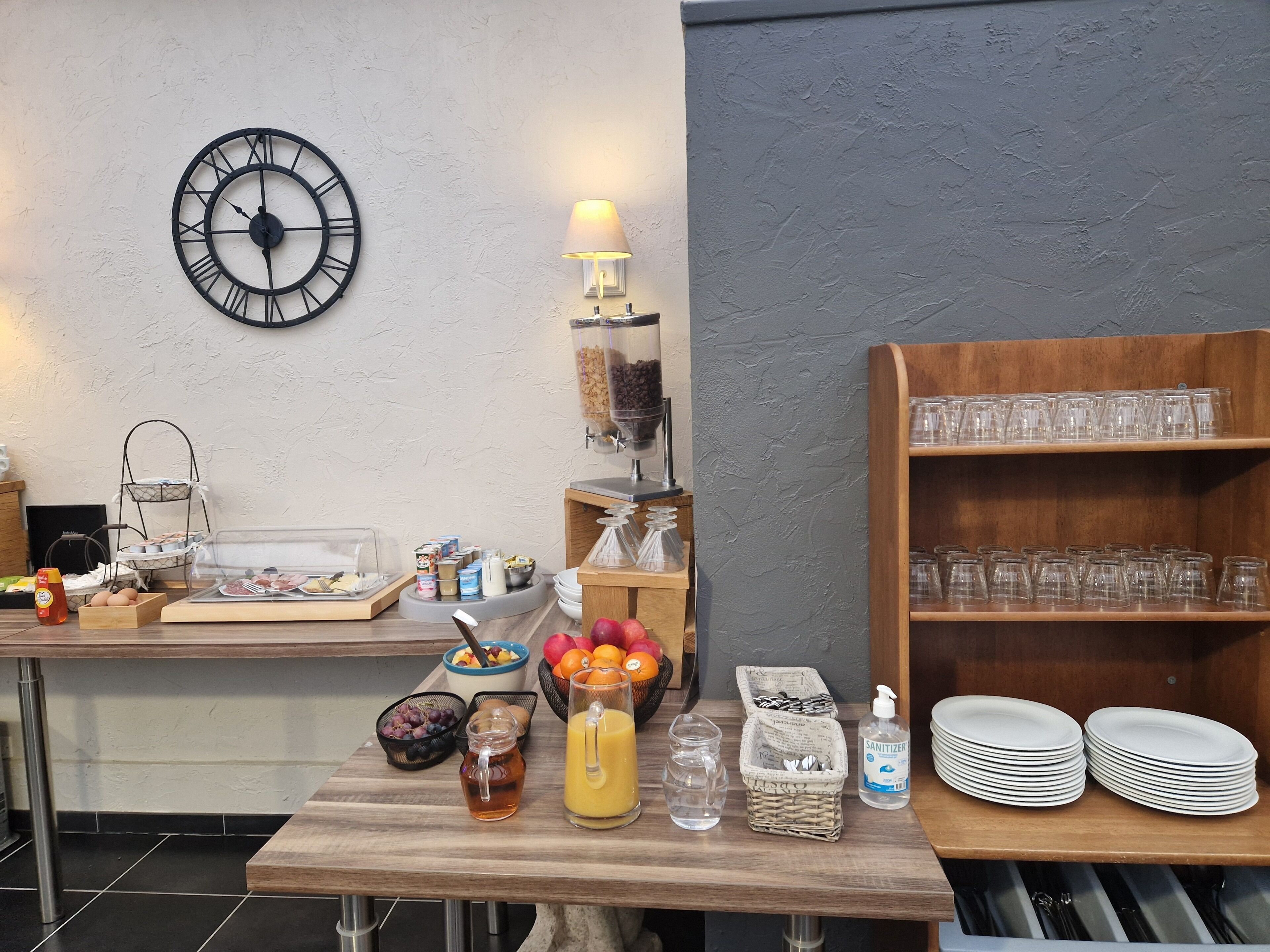 Een ontbijtsetting met een klok, een lamp en diverse etens- en drankjes op een tafel.