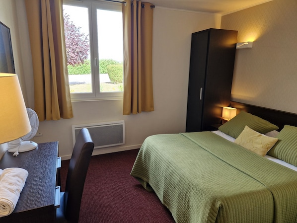 Habitación de hotel con cama, escritorio con lámpara, silla, armario y ventana con cortinas.