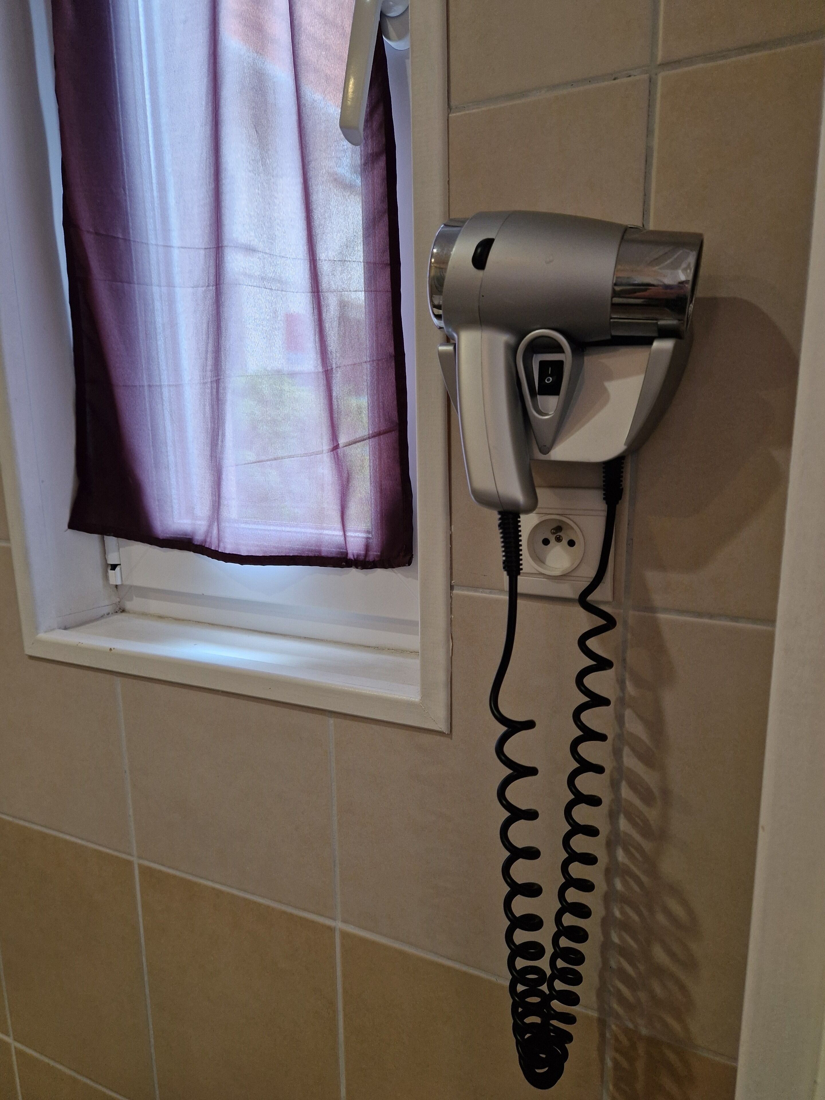 A hair dryer mounted on a wall near a window with a curtain.
